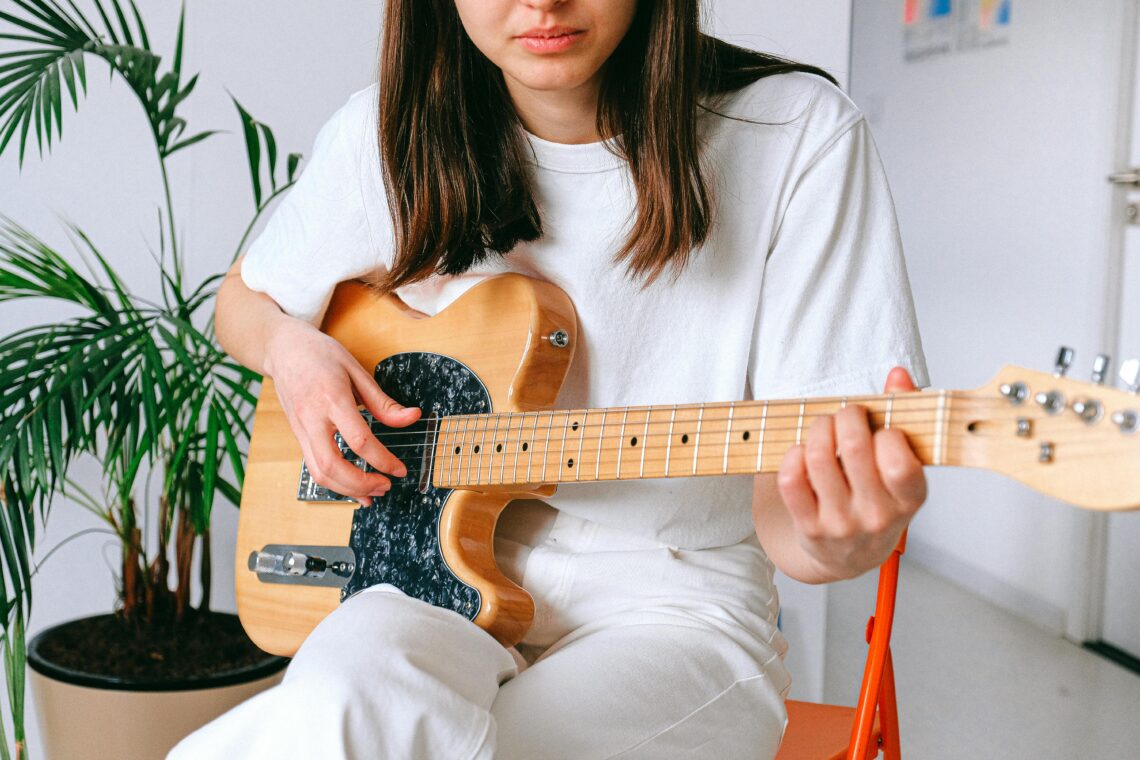 A woman in a white outfit playing an electric guitar indoors, enjoying leisure time.