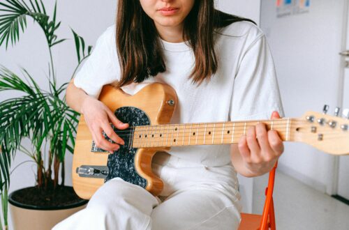 A woman in a white outfit playing an electric guitar indoors, enjoying leisure time.