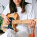 A woman in a white outfit playing an electric guitar indoors, enjoying leisure time.