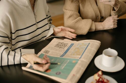Elderly women discussing a newspaper crossword while enjoying coffee indoors.