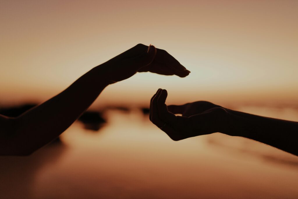 Silhouette of two hands reaching out at sunset, symbolizing connection and support and energy healing.