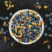 Top-down view of a bowl filled with fresh blueberries, pecans, and yellow raisins on a dark textured background.