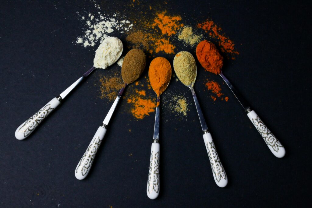 Colorful assortment of cumin and other spices displayed on ornate spoons against a dark background, showcasing culinary variety.