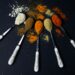 Colorful assortment of flavor in spices displayed on ornate spoons against a dark background, showcasing culinary variety.
