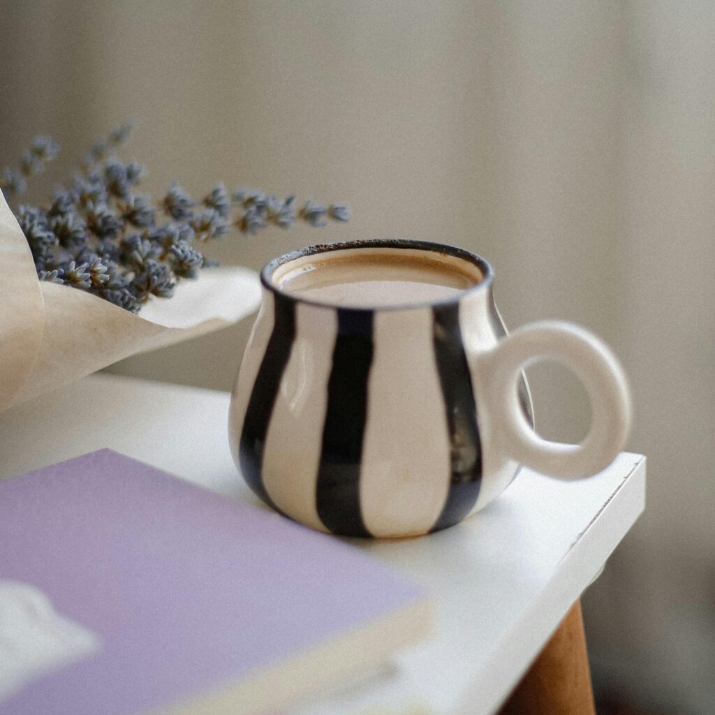 A striped mug of coffee with lavender and a book on a table, evoking a warm, cozy atmosphere.