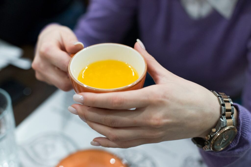 Close-up of hands holding a cup filled with a bright yellow beverage, creating a warm and inviting scene.