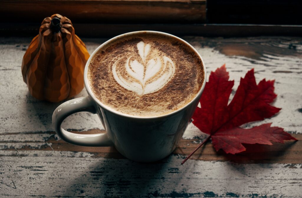 Warm cappuccino with latte art beside a red maple leaf on a rustic table