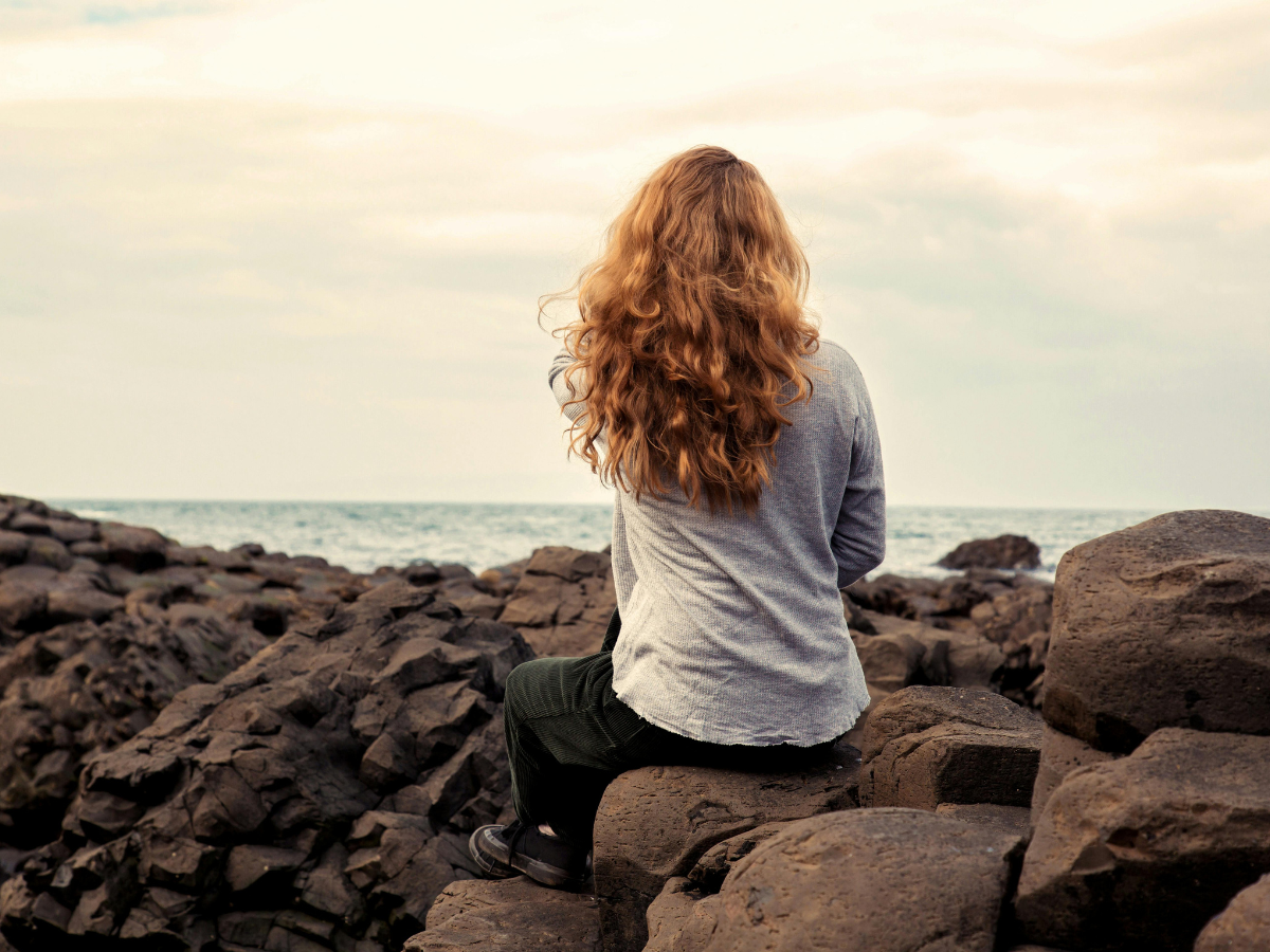 woman sitting on the rocks, woman in deep thought, admiring the water