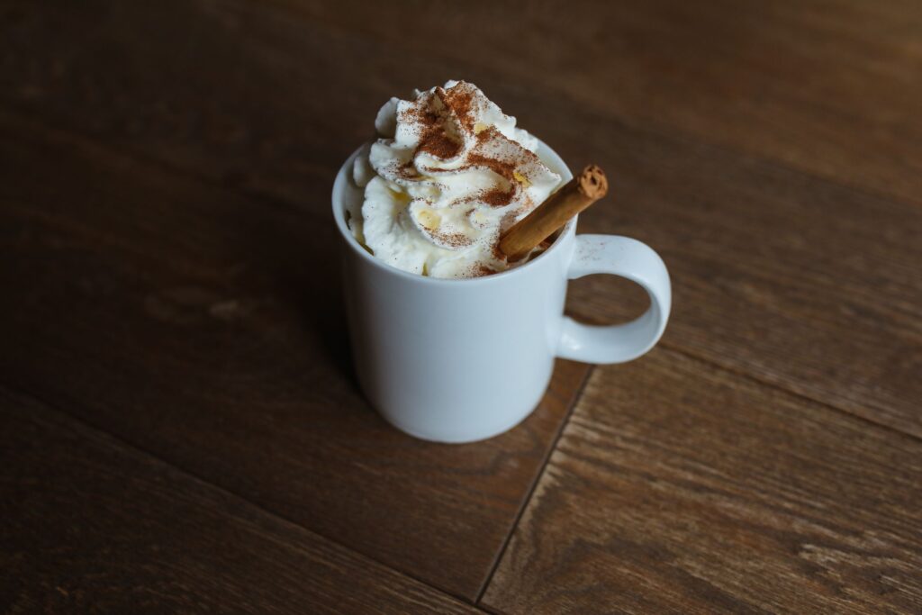 A delicious cinnamon latte topped with whipped cream served in a white mug on a wooden table. Photo by by Polina Tankilevitch via pexels
